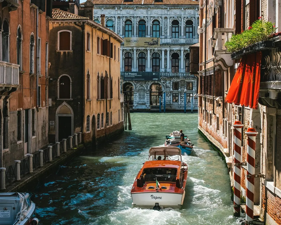 A wooden water taxi on a quiet Venetian canal, Ca’ Pesaro on the Grand Canal ahead.